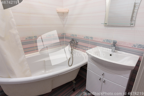 Image of Interior of a cozy ordinary bathroom with a washbasin, a bathtub and a mirror