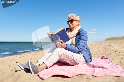 Image of happy senior woman reading book on summer beach