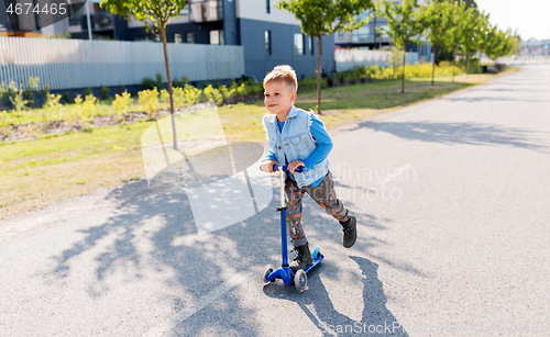 Image of happy little boy riding scooter in city