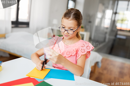 Image of girl cutting color paper with scissors at home