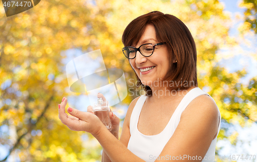 Image of smiling senior woman spraying perfume to her wrist