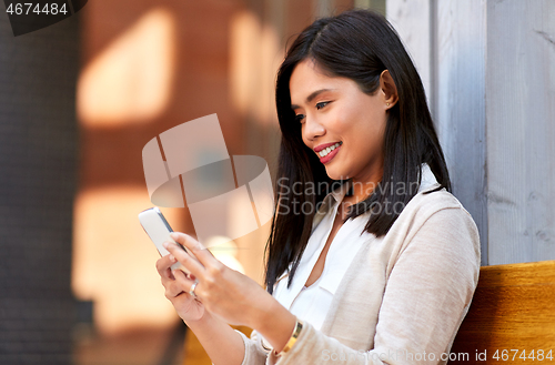 Image of asian woman using smartphone sitting on bench