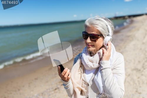 Image of old woman in headphones with smartphone on beach