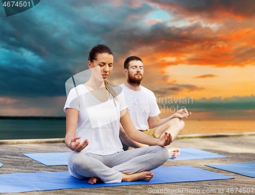 Image of couple meditating in yoga lotus pose outdoors
