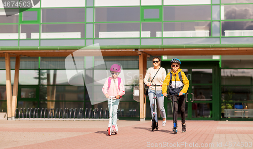 Image of happy school children with mother riding scooters