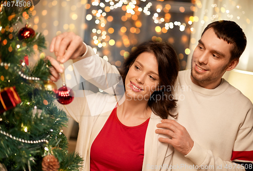 Image of happy couple decorating christmas tree at home