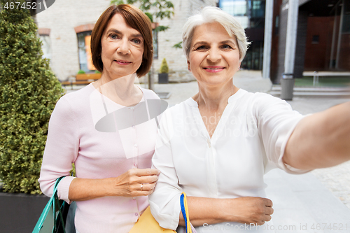 Image of old women with shopping bags taking selfie in city