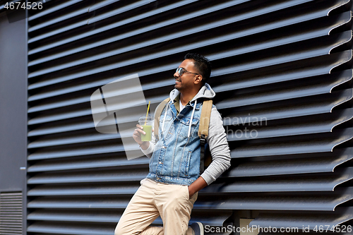 Image of man with backpack drinking smoothie on street