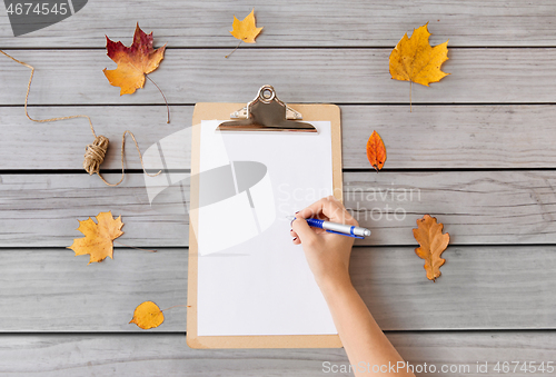 Image of hand writing on white paper on clipboard in autumn