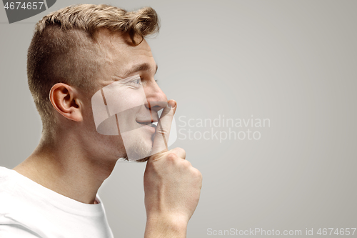 Image of Keep silence. Handsome young man in white shirt looking at camera and holding finger on lips