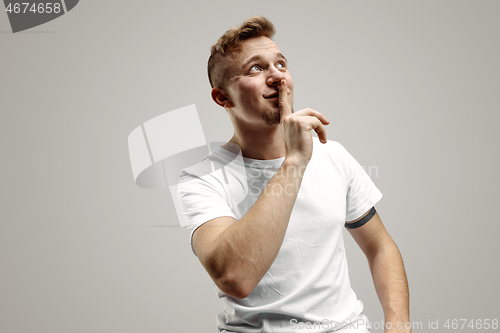 Image of Keep silence. Handsome young man in white shirt looking at camera and holding finger on lips