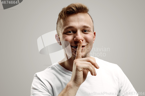 Image of Keep silence. Handsome young man in white shirt looking at camera and holding finger on lips