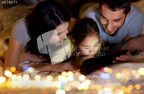 Image of family with tablet pc in bed at night at home