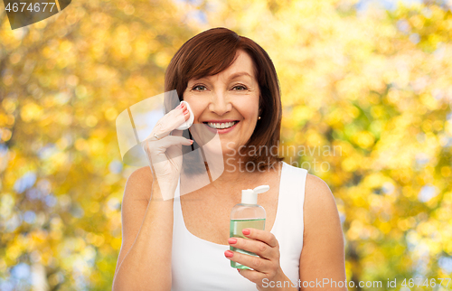 Image of senior woman cleaning face by lotion on cotton pad