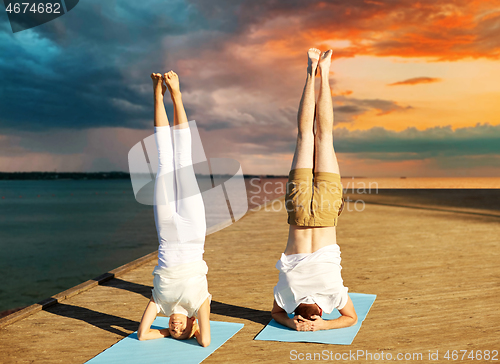 Image of couple making yoga headstand on mat outdoors