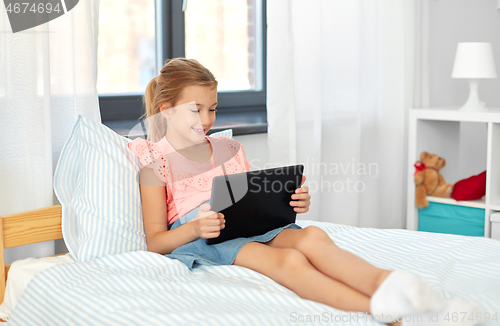 Image of smiling girl with tablet pc sitting on bed at home