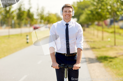 Image of businessman with headphones riding scooter in city