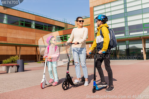 Image of happy school children with mother riding scooters