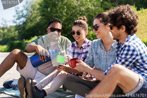 Image of happy friends drinking tea from thermos in summer