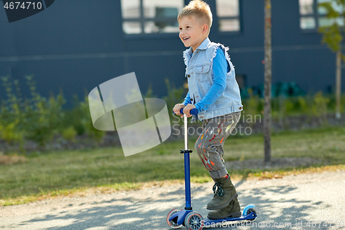 Image of happy little boy riding scooter in city