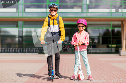 Image of happy school children in helmets riding scooters