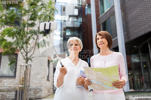 Image of senior women with map and city guide taking selfie