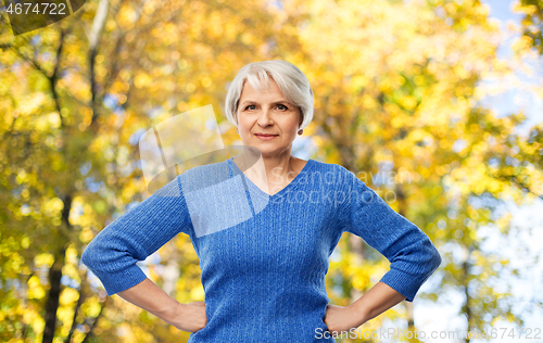 Image of senior woman with hands on hips in autumn park