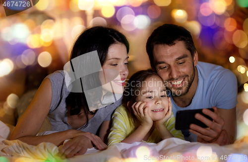 Image of happy family with smartphone in bed at night