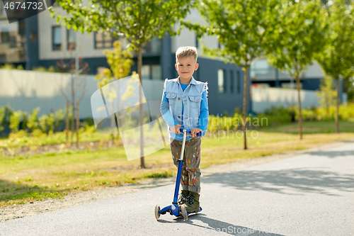 Image of happy little boy riding scooter in city