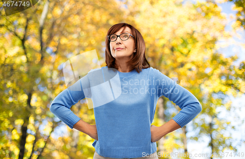 Image of angry senior woman in glasses over autumn park