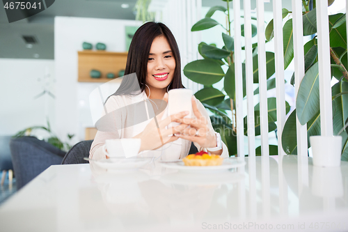 Image of asian woman with smartphone and earphones at cafe