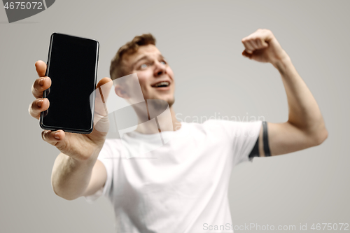 Image of Young handsome man showing smartphone screen isolated on gray background in shock with a surprise face