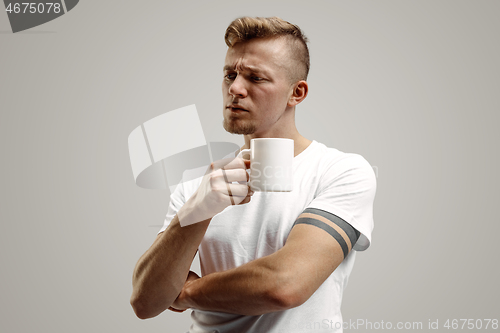 Image of Taking a coffee break. Handsome young man holding coffee cup while standing against gray background