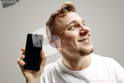 Image of Young handsome man showing smartphone screen isolated on gray background in shock with a surprise face