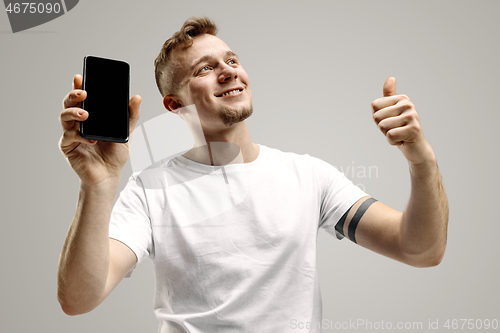 Image of Young handsome man showing smartphone screen isolated on gray background in shock with a surprise face