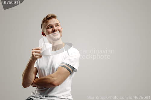 Image of Taking a coffee break. Handsome young man holding coffee cup, smiling while standing against gray background