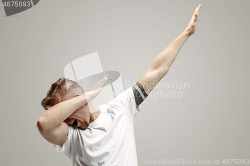 Image of Young man makes the dab movement with his arms on a gray background.