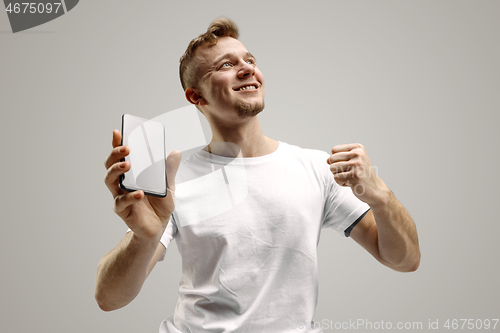 Image of Young handsome man showing smartphone screen isolated on gray background in shock with a surprise face