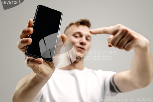 Image of Young handsome man showing smartphone screen isolated on gray background in shock with a surprise face