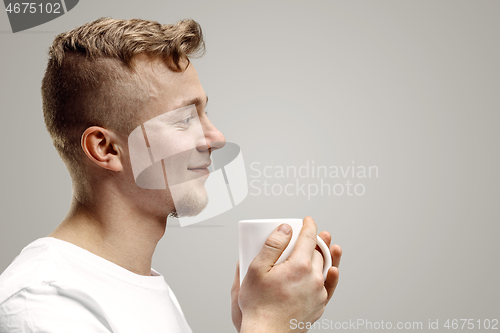 Image of Taking a coffee break. Handsome young man holding coffee cup, smiling while standing against gray background