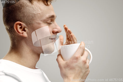 Image of Taking a coffee break. Handsome young man holding coffee cup, smiling while standing against gray background