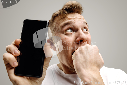 Image of Young handsome man showing smartphone screen isolated on gray background in shock with a surprise face