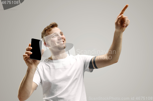 Image of Young handsome man showing smartphone screen isolated on gray background in shock with a surprise face