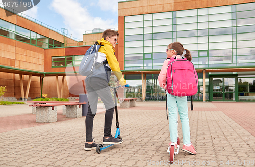 Image of happy school children with backpacks and scooters