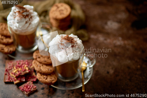 Image of Two tall glasses with hot chocolate, whipped cream and cinnamon powder on top