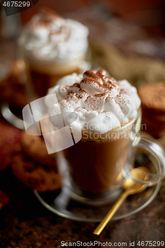 Image of Two tall glasses with hot chocolate, whipped cream and cinnamon powder on top