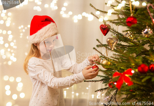 Image of happy girl in santa hat decorating christmas tree