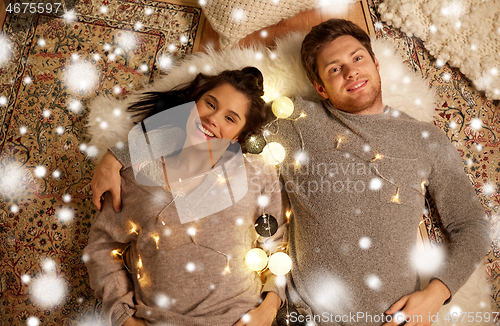 Image of happy couple with garland lying on floor at home