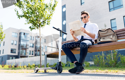 Image of businessman with scooter reading newspaper in city