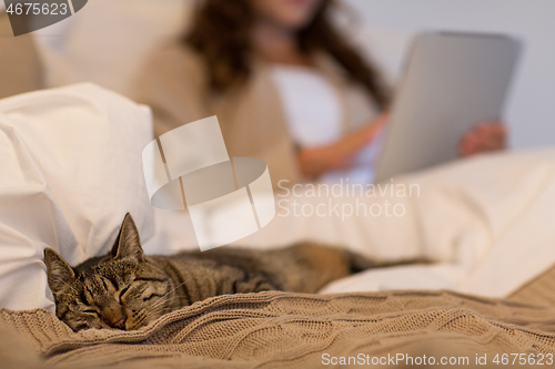 Image of tabby cat sleeping in bed with woman at home